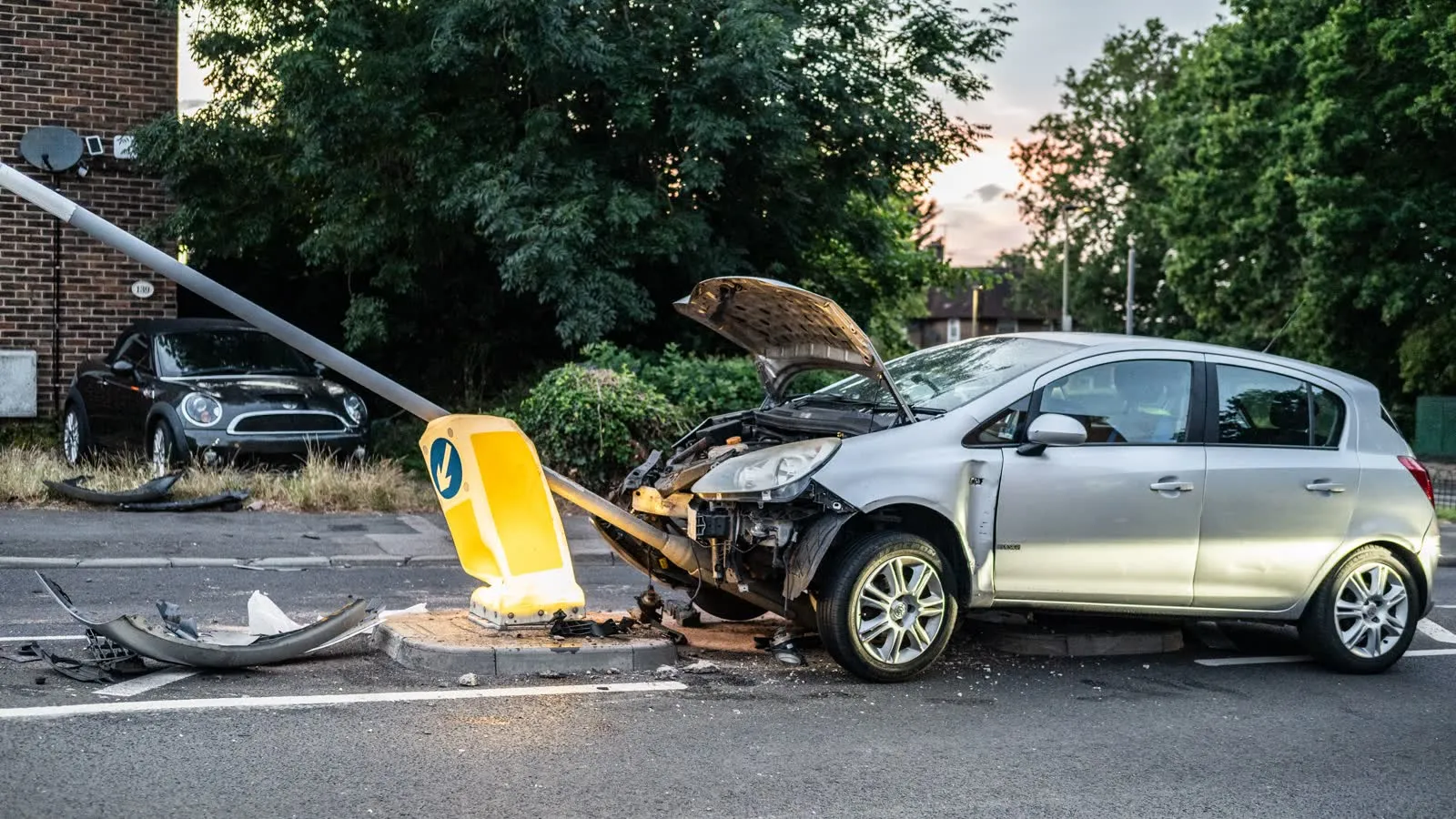 A damaged car after a collision with a street lamp post at dusk.