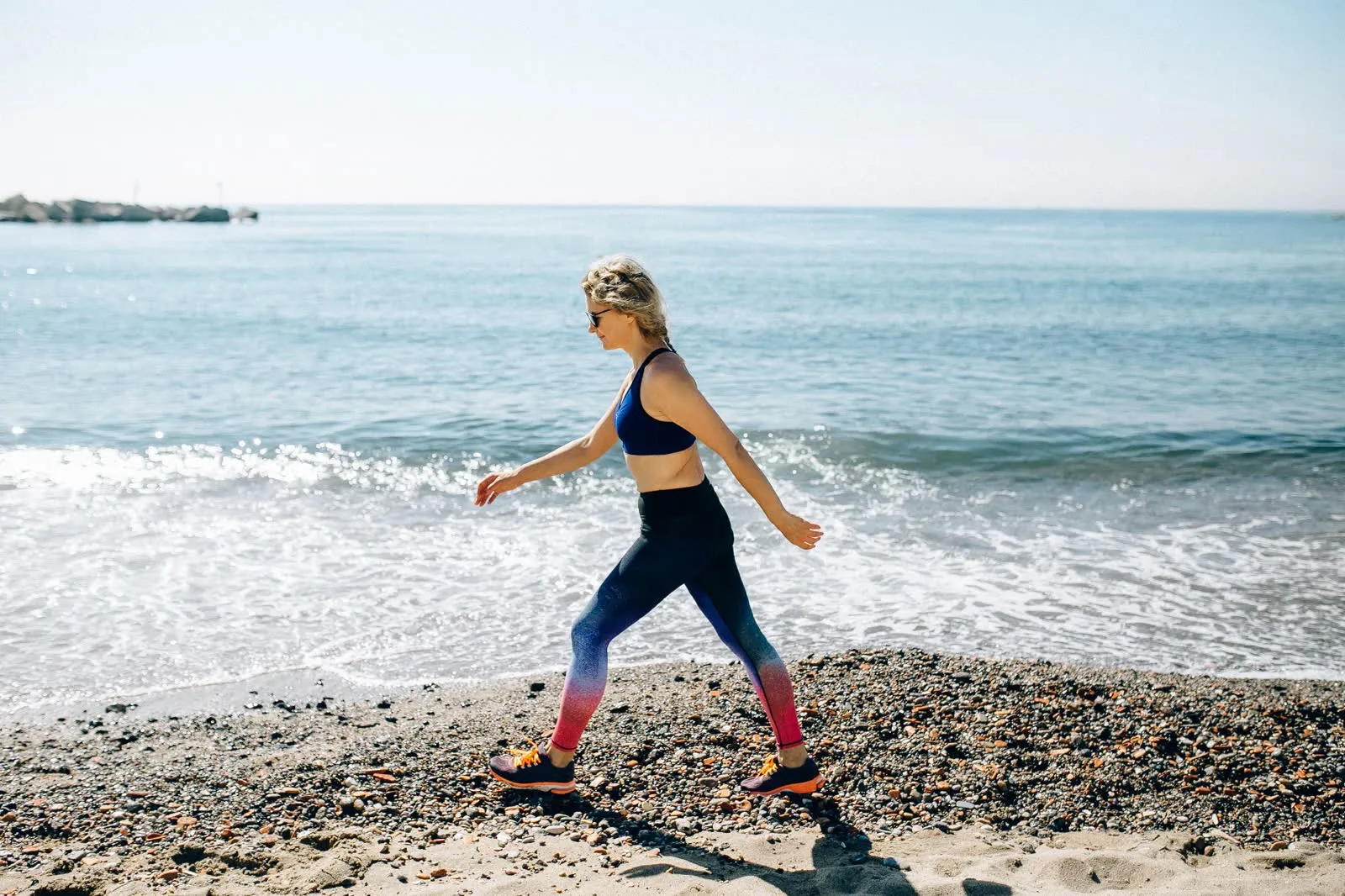 A woman walking along the shoreline of a beach.